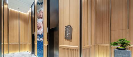 A modern elevator interior with a directory sign, wooden paneling, and a potted plant.