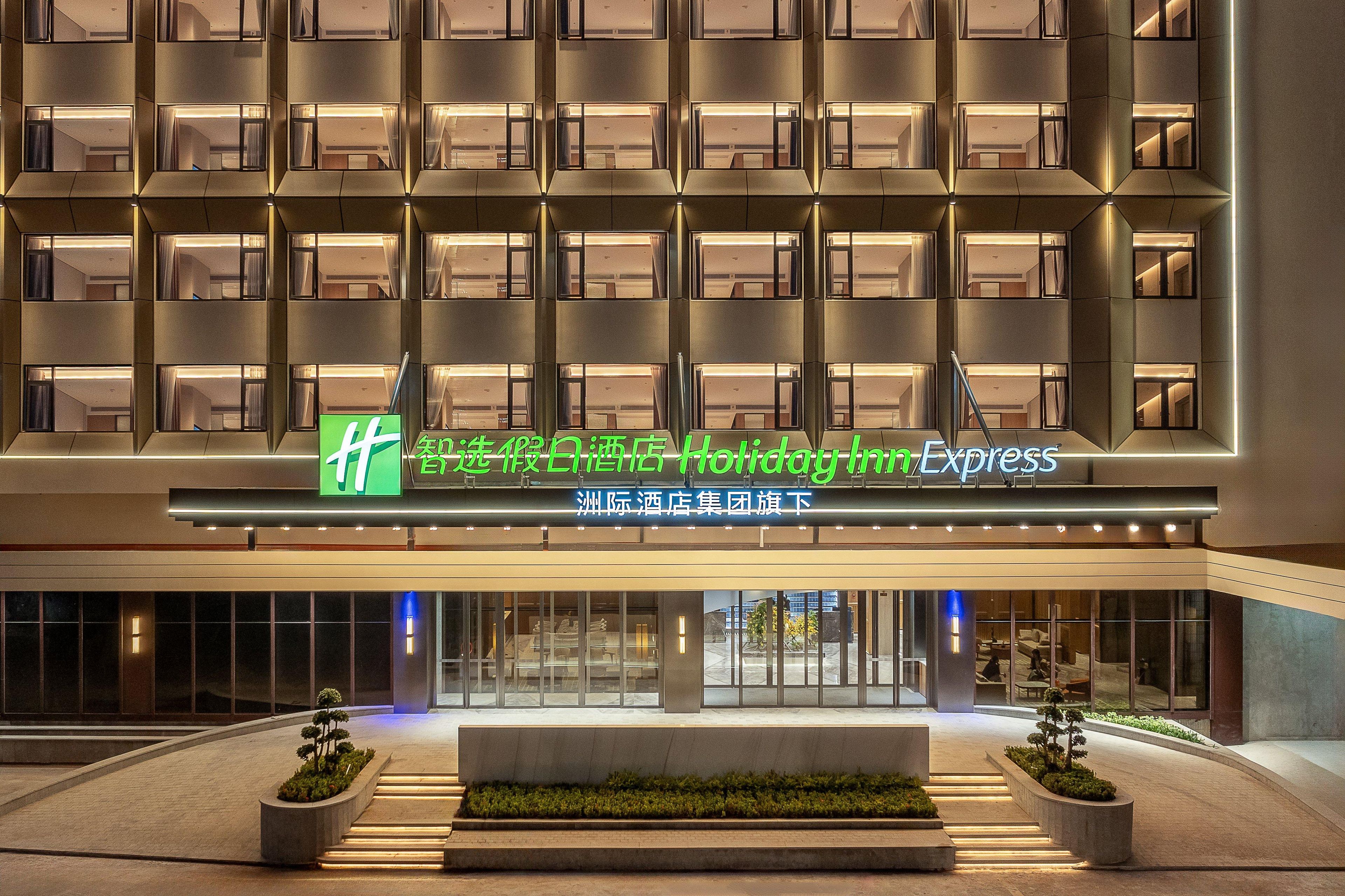 A hotel entrance with a modern facade, multiple balconies, and a sign indicating a Holiday Inn Express.