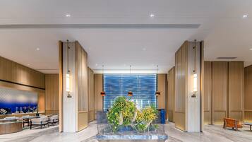 Een moderne lobby met een marmeren receptiebalie, een zithoek en een centraal bloemenarrangement.