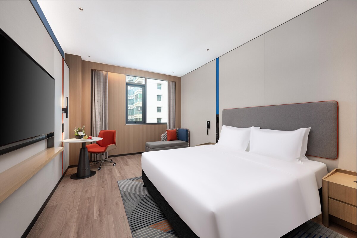 A modern hotel room with a large bed, a desk, a chair, and a TV.