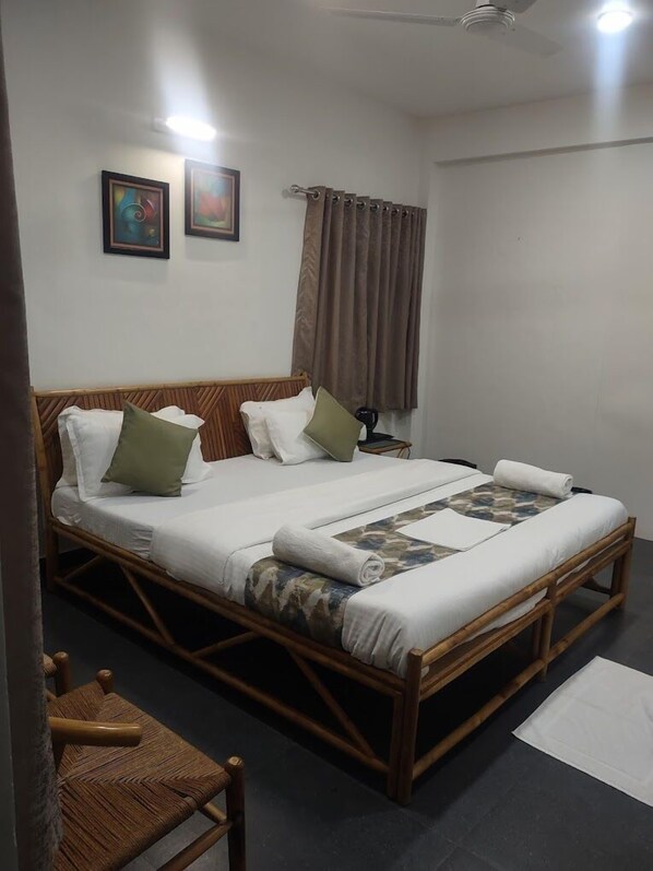 A single bed with a wooden frame, white bedding, and a patterned throw. There is a nightstand with a lamp, a chair, and a window with curtains. - Fame Food Sayla (Sayla)