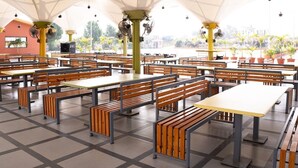 Un amplio espacio de comedor al aire libre con varias mesas y bancos, grandes sombrillas que brindan sombra y vistas del paisaje circundante.