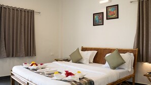 Una cama bien tendida con estructura de madera, ropa de cama blanca y almohadones decorativos. Se observan dos cuadros enmarcados en la pared sobre la cama.
