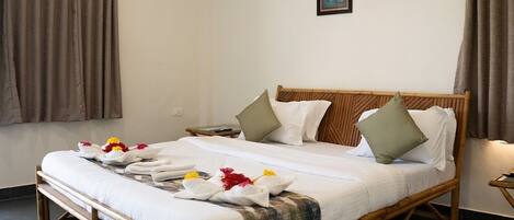 Una cama bien tendida con estructura de madera, ropa de cama blanca y almohadones decorativos. Se observan dos cuadros enmarcados en la pared sobre la cama.