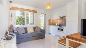 Ein modernes Wohnzimmer mit grauem Sofa, einem Holzesstisch und einer Küchenzeile mit weißen Schränken und einem Herd.