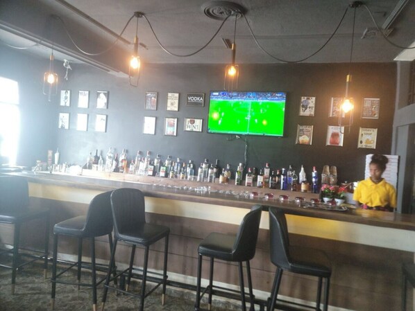A bar area with a counter, multiple bottles of alcohol, and framed pictures on the wall. - Canaan bed & breakfast (Addis Ababa)