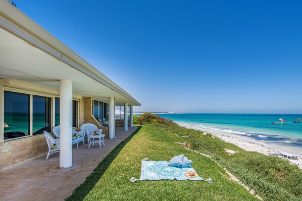 A beachside patio with a view of the ocean, a grassy area, and a covered seating area with chairs.