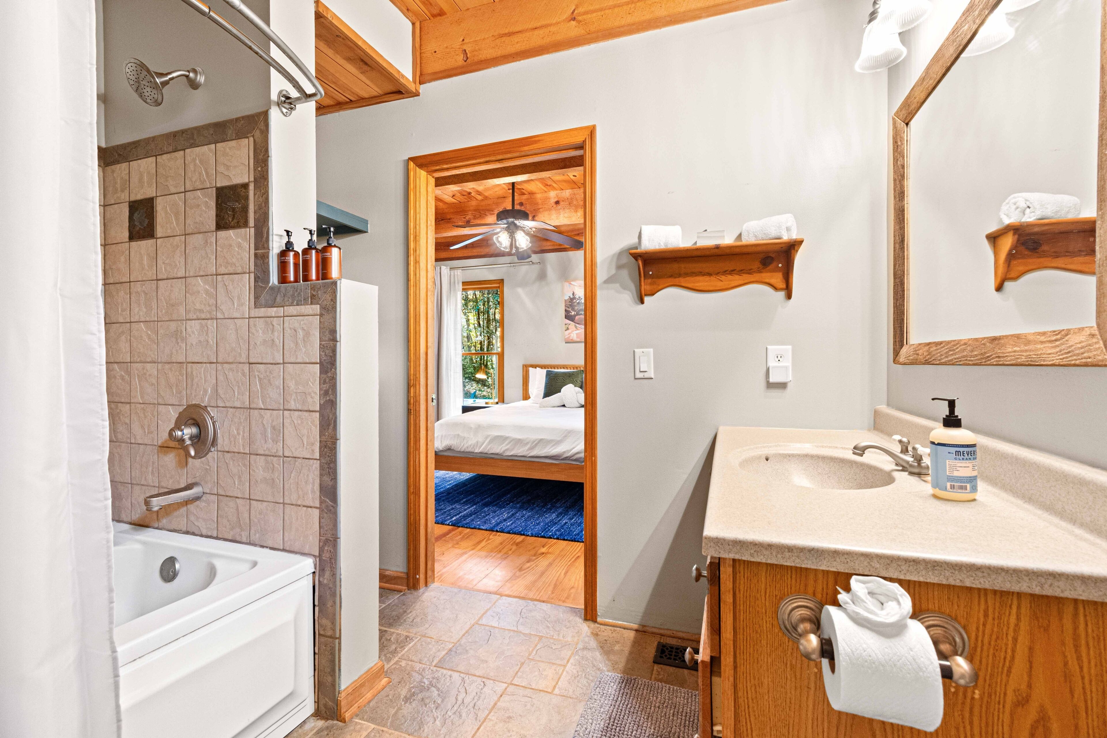 A bathroom with a bathtub, shower, and sink. There is a wooden shelf with towels and a mirror above the sink.