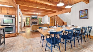 A spacious kitchen with wooden beams, a dining area with blue chairs, and a staircase leading to another level.