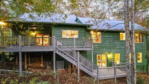 A green wooden house with a balcony and a staircase leading to the upper floor.