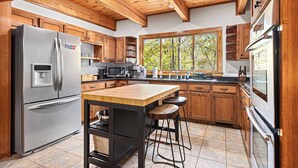 A modern kitchen with wooden cabinets, stainless steel appliances, and a large window.