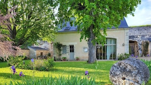 A traditional stone building with a large tree in the foreground, a well-maintained garden with various plants, and a clear view of the building's entrance. - Le Plessis-Lepage - "Le Gite" **** Calm-Space-Green at Azay-Le-Rideau (Azay-le-Rideau)