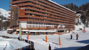 A multi-story hotel with balconies, a ski slope in the background, and a clear blue sky. - Ski-in/ski-out & foot of the slopes, 9th floor, view ski slopes, balcony, tv, 24m², La Plagne (La Plagne)