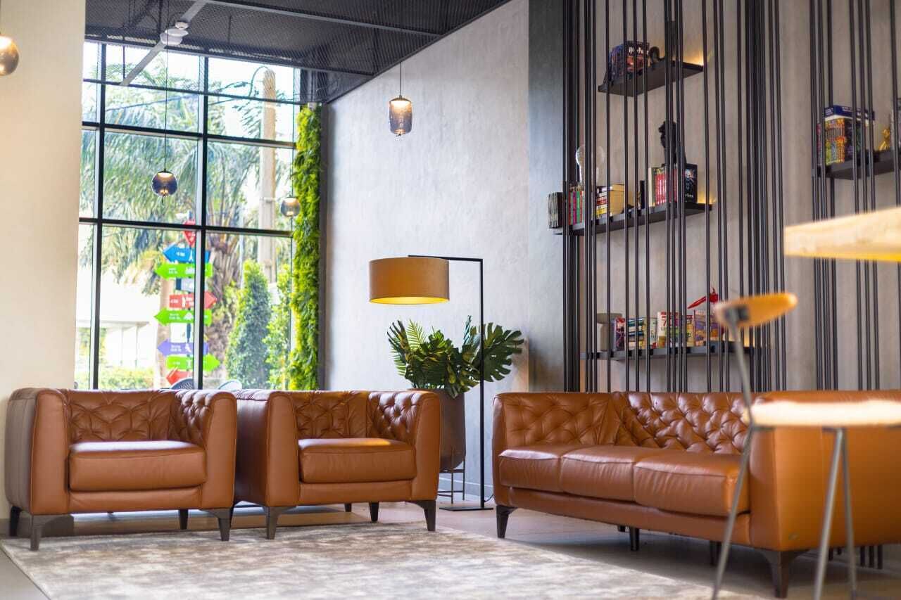 A modern living room with leather sofas, a floor lamp, and a bookshelf with decorative items.