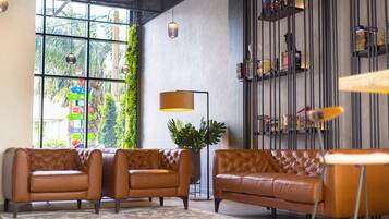 A modern living room with leather sofas, a floor lamp, and a bookshelf with decorative items.