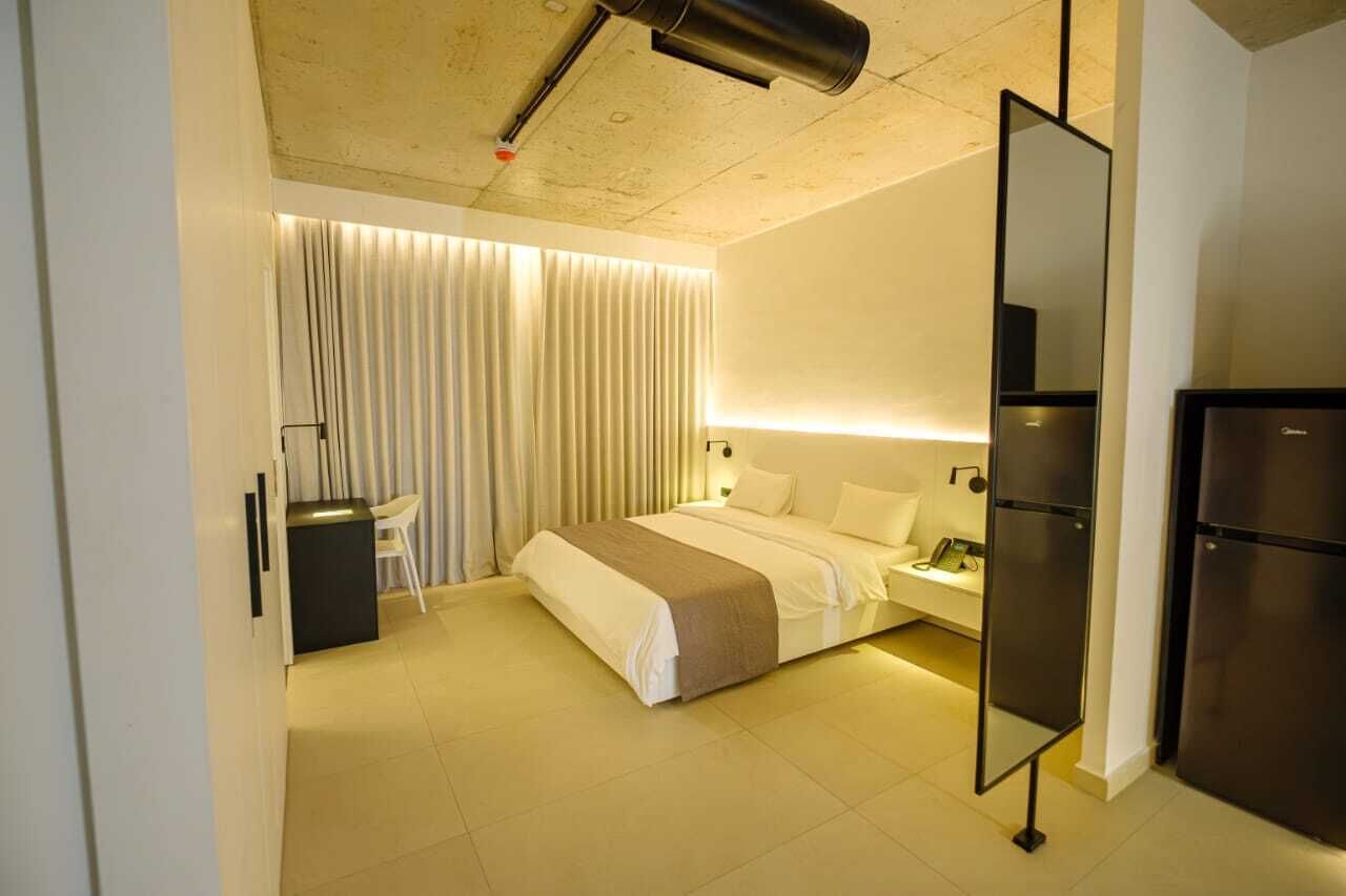 A modern hotel room with a bed, bedside table, and a built-in refrigerator.