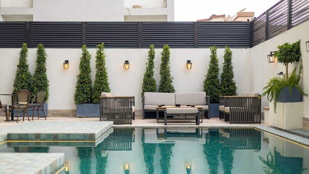 Un área junto a la piscina con mobiliario, una piscina pequeña y vegetación vertical.