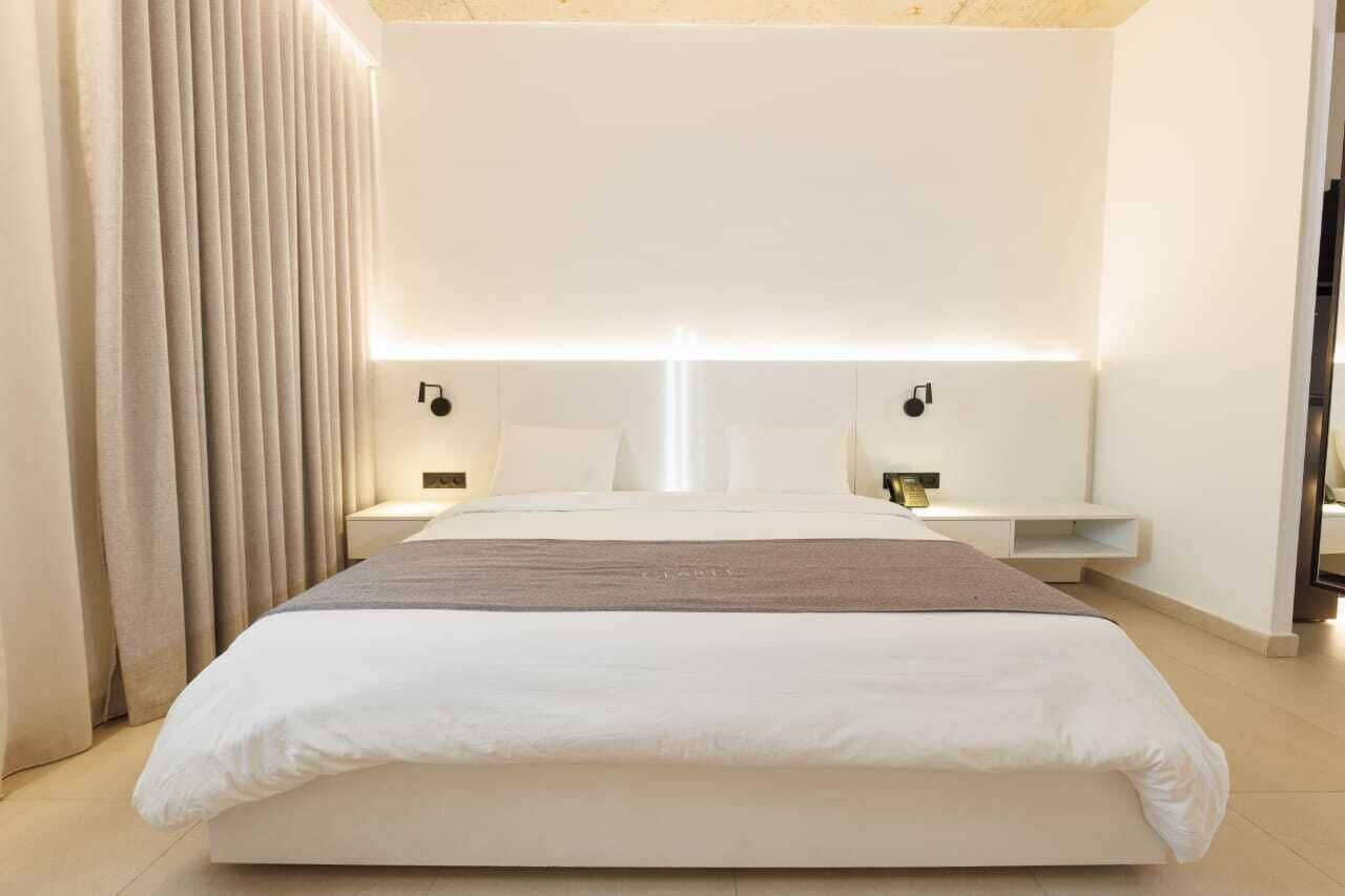 A modern hotel room with a large bed, bedside tables, and a headboard with integrated lighting.
