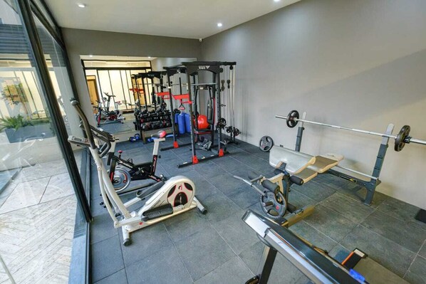 Un gimnasio con equipo de ejercicio variado, que incluye una cinta de correr, un banco de pesas y una estructura para sentadillas.