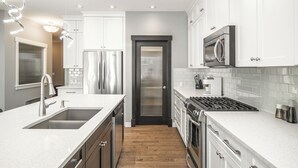 A modern kitchen with stainless steel appliances, white cabinetry, and a wooden floor.