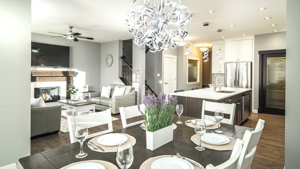A modern kitchen with white cabinets, a stainless steel refrigerator, and a dining area set for six with a dark wood table and white chairs.
