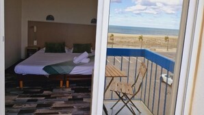 Un dormitorio con cama, almohadas y vista a la playa desde un balcón.