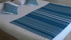 Una cama con una colcha azul y blanca a rayas, dos almohadas, una mesita de noche y una lámpara de pared.
