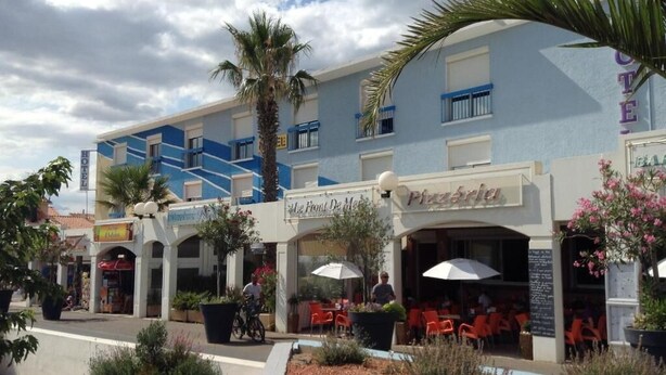 Un hotel con terraza al aire libre, palmeras y fachada azul.