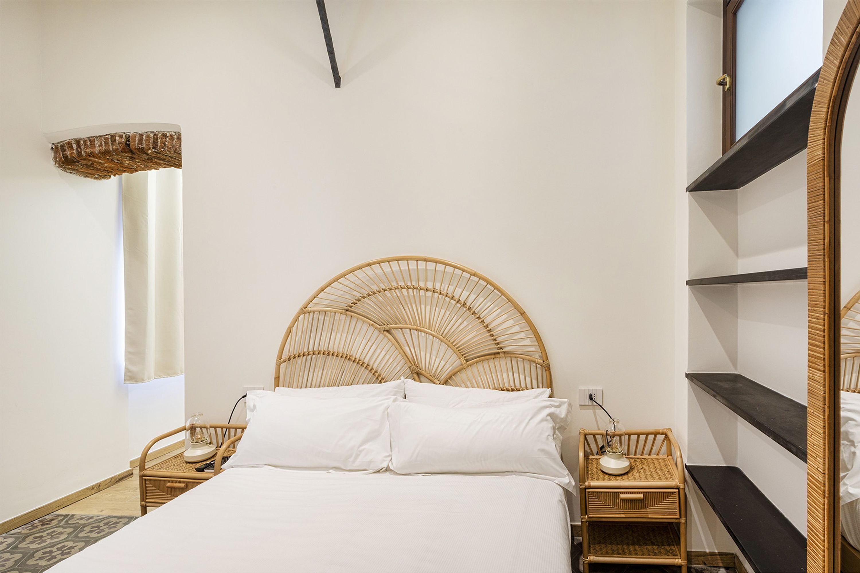 Ein Schlafzimmer mit einem großen Bett, zwei Nachttischen, einem Rattan-Kopfstück und eingebauten Regalen.