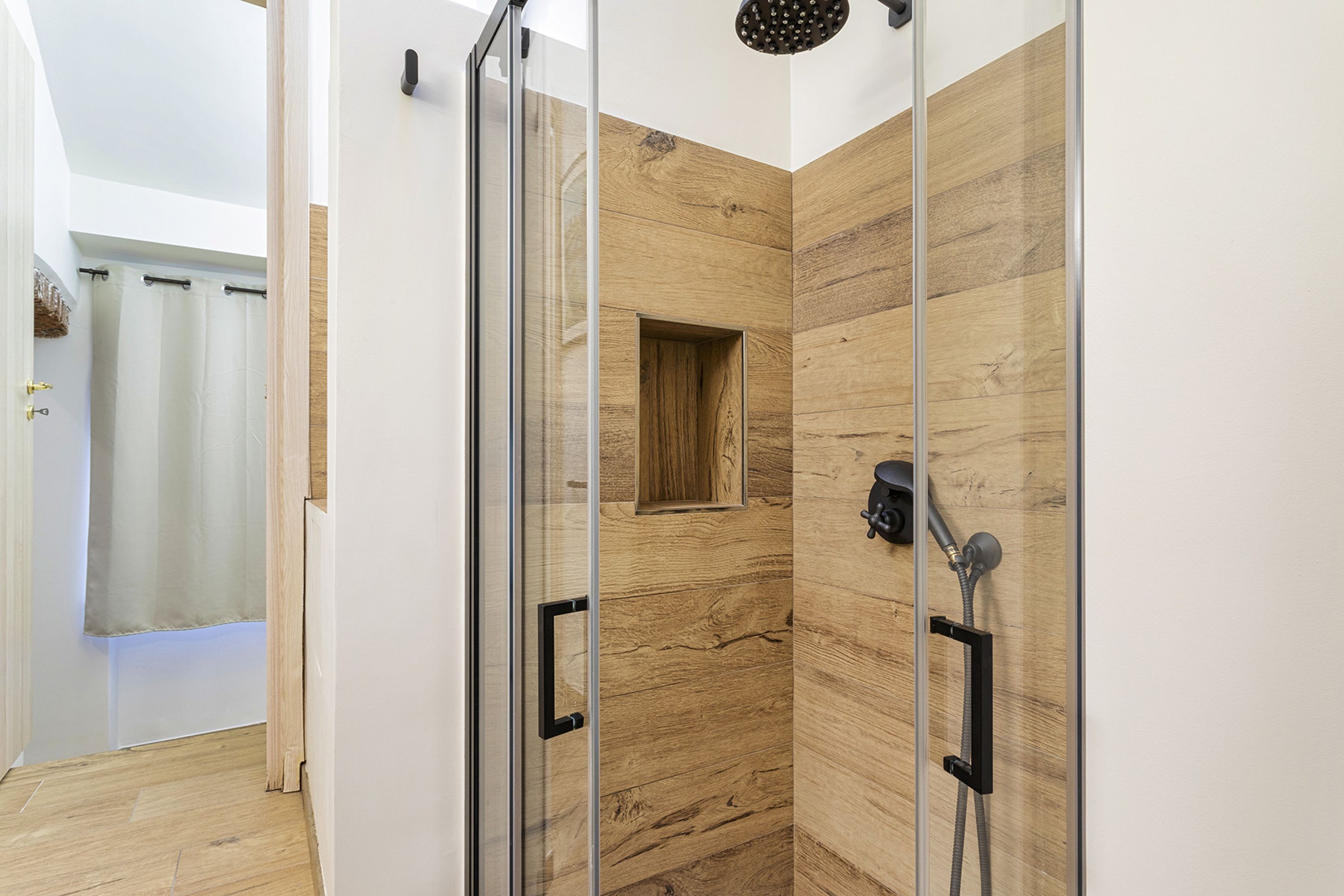 A modern shower with glass doors, a wooden panel wall, and a showerhead.