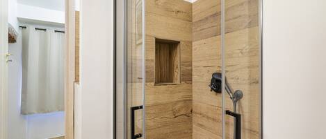 A modern shower with glass doors, a wooden panel wall, and a showerhead.