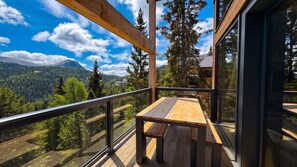 A wooden deck with a table and chairs, overlooking a forested valley and mountains. - Superior Chalet # 25 with Sauna (Turrach)