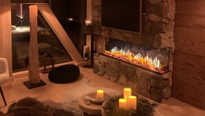 A stone fireplace with a TV mounted above it, surrounded by candles and a rustic wooden bench. - Superior Chalet # 25 with Sauna (Turrach)