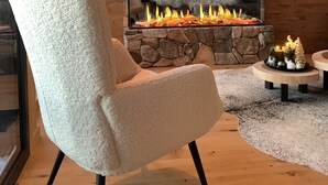 A modern living room with a stone fireplace, a comfortable armchair, a floor lamp, and a small table with candles. - Superior Chalet # 25 with Sauna (Turrach)