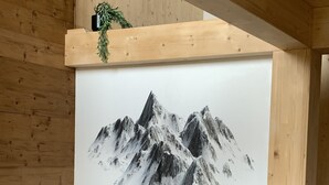 A room with a large painting of snow-capped mountains on the wall, a wooden ceiling, and a grey sofa. - Superior Chalet # 25 with Sauna (Turrach)
