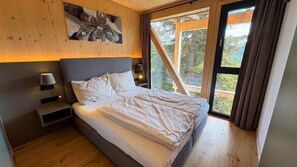 A bedroom with a bed, nightstands, a wall-mounted lamp, and a window with curtains.