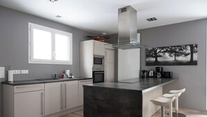 Una cocina moderna con una isla central, taburetes de bar y un ventanal amplio.