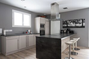 A modern kitchen with a central island, bar stools, and a large window.