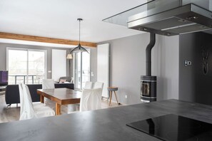 A modern kitchen with a central island, a built-in stove, and a dining area with chairs and a table.