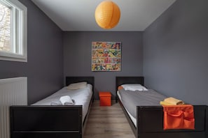 A room with two beds, a radiator, a window, and a colorful poster on the wall.