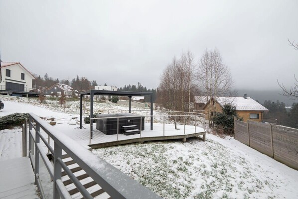 A snow-covered outdoor area with a wooden deck, a metal railing, and a bench.