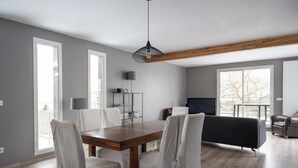Una sala de estar moderna con una mesa de comedor de madera, sillas blancas, un sofá negro y un televisor.
