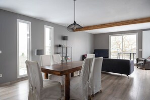 A modern living room with a wooden dining table, white chairs, a black sofa, and a television.