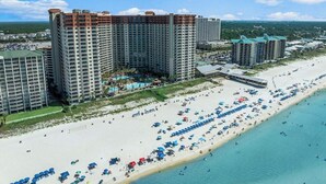 A beachfront hotel with multiple high-rise buildings, a sandy beach with numerous umbrellas, and a clear view of the ocean.