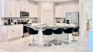 Una cocina moderna con armarios blancos, electrodomésticos de acero inoxidable y una isla central con taburetes de bar.