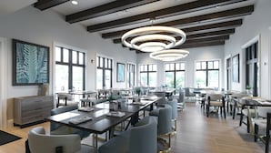 Un comedor amplio con varias mesas y sillas, ventanas grandes e iluminación colgante moderna.