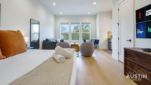 Una habitació d'hotel moderna amb un llit gran, una zona de seients amb un sofà i cadires, una taula petita i un televisor que mostra serveis de transmissió.
