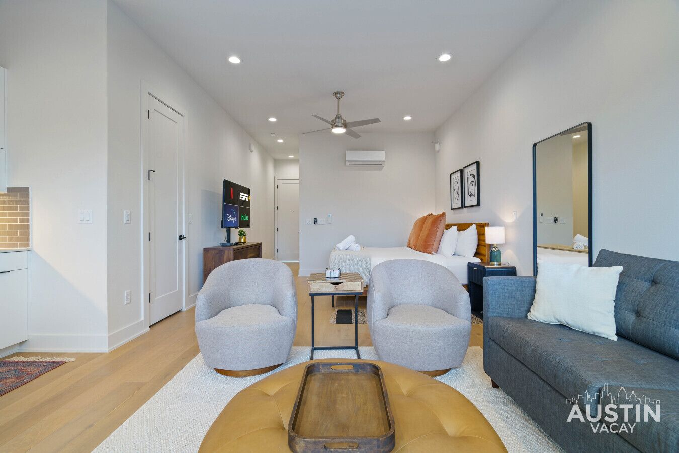 A modern hotel room with a bed, two armchairs, a sofa, a small table, and a television.