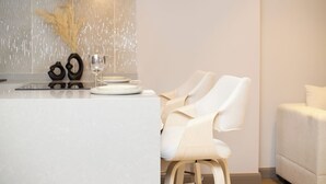 A modern kitchen with a marble countertop, two white chairs, and a white sofa. - Luxury 1-bedroom apartment in Diamond in the City in Cantonments  (Accra)