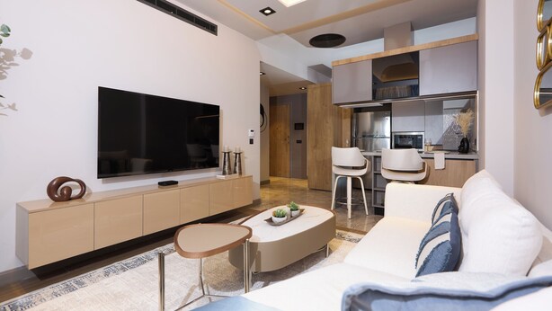 A modern living room with a flat-screen TV, a sofa, a coffee table, and a kitchen area in the background. - Luxury 1-bedroom apartment in Diamond in the City in Cantonments  (Accra)